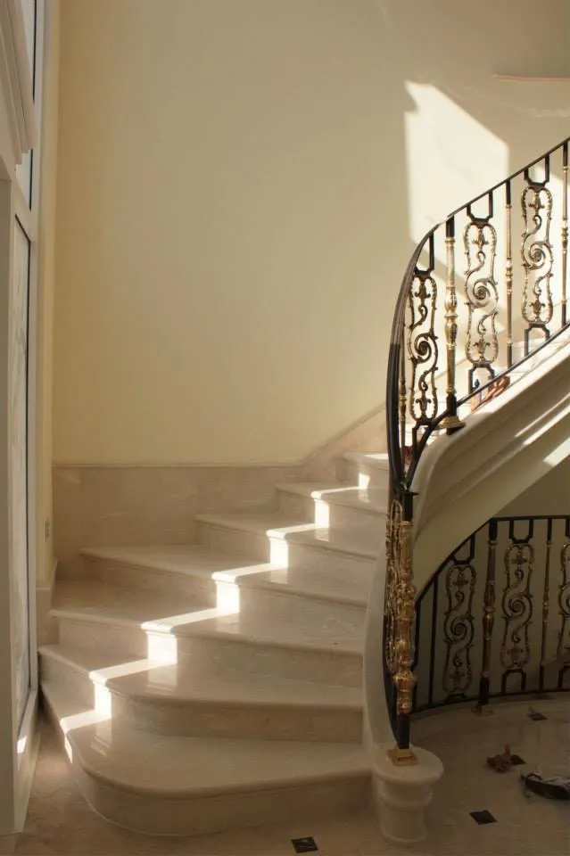 Escalier courbe en pierre claire avec rampe en fer forgé